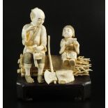 A Japanese ivory okimono of a woodsman sitting on a bundle of twigs with a young child,