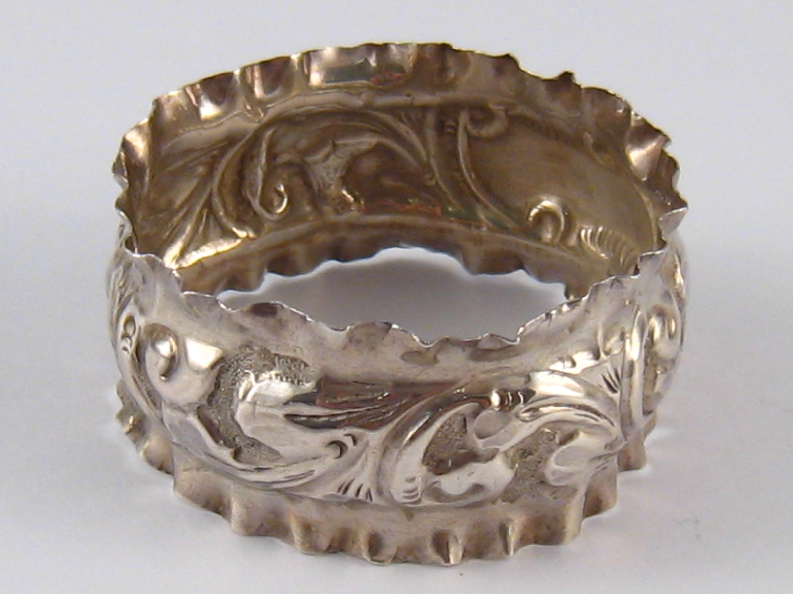 A silver napkin ring with scrolling and crimped sides. Birmingham, 1907.