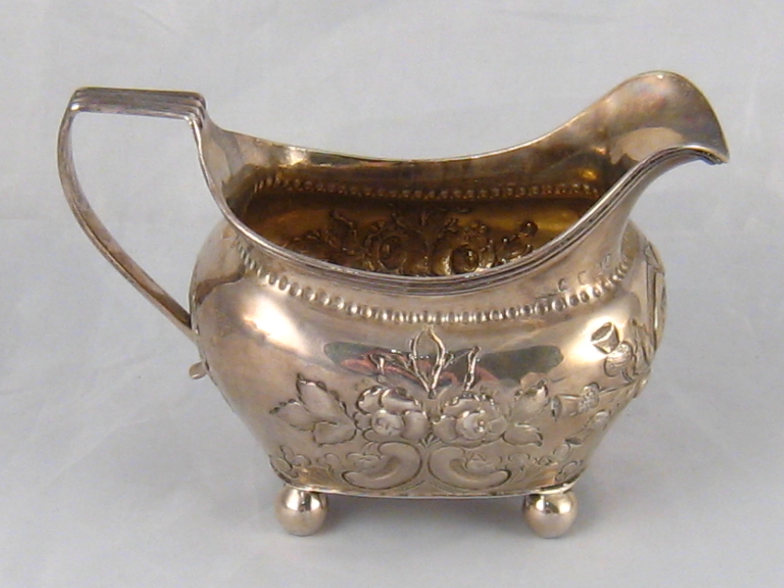 A Georgian silver cream jug on ball feet with reeded rim and later embossing, by Thomas Johnson,