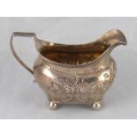 A Georgian silver cream jug on ball feet with reeded rim and later embossing, by Thomas Johnson,