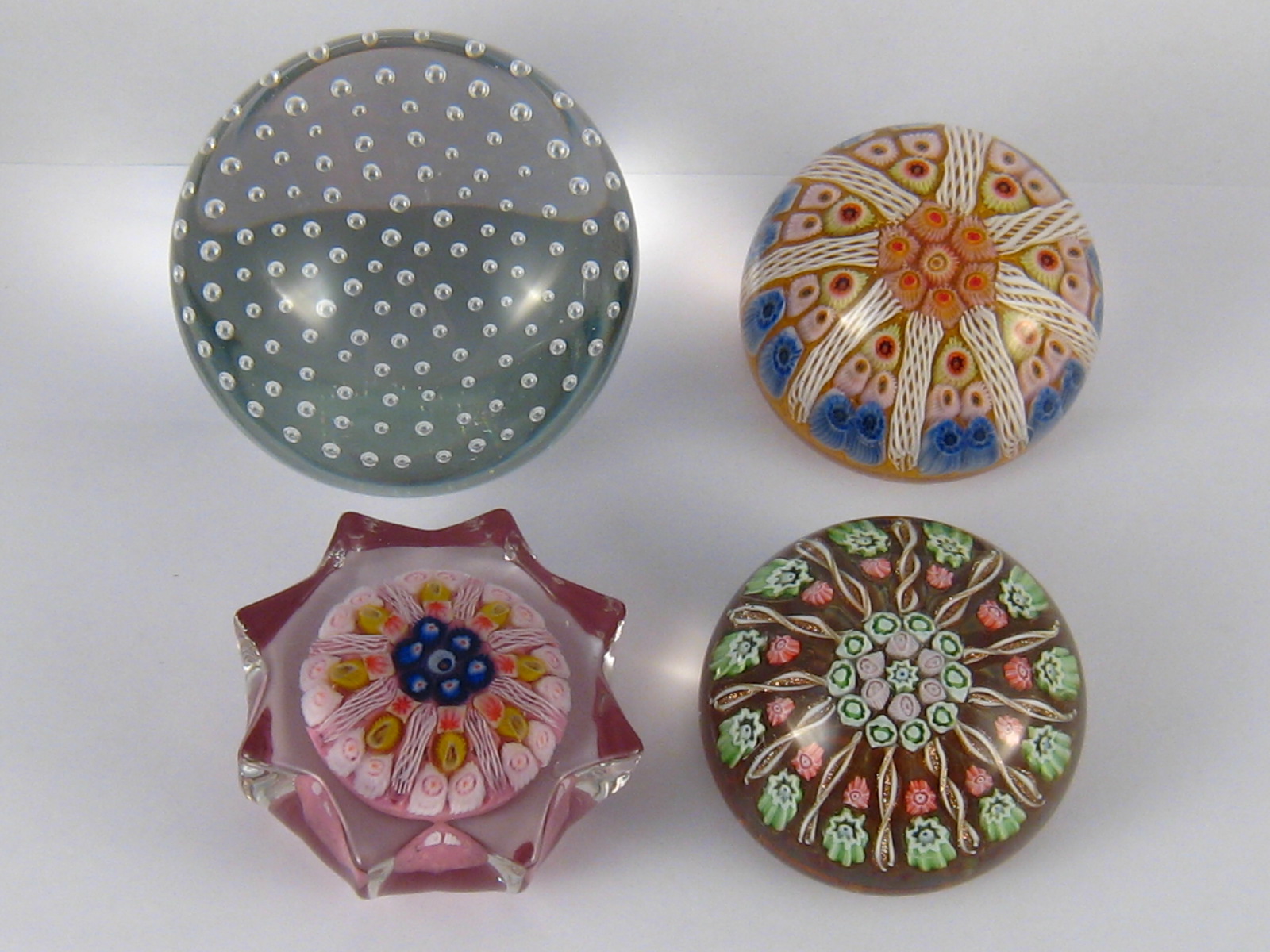 Four glass paperweights, one clear with symmetrical bubbles, three cushion with millefiore canes ,