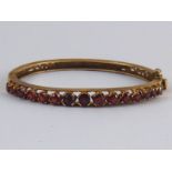 A 9 carat gold garnet bracelet, internal width approx 57mm, width of bangle approx 6mm, 16 gms.