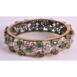 AN UNUSUAL EARLY 20TH CENTURY INDIAN GILDED PASTE AND EMERALD BANGLE. 2.75ins diameter.