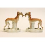 A PAIR OF VICTORIAN STAFFORDSHIRE POTTERY GREYHOUNDS, modelled standing with hares in their