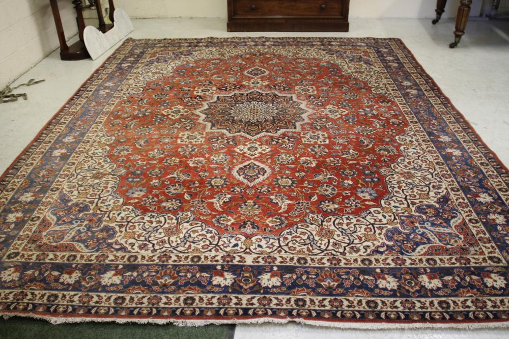 A PERSIAN CARPET, the red floral field with central navy blue gul and ivory spandrel, blue foliate