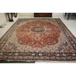 A PERSIAN CARPET, the red floral field with central navy blue gul and ivory spandrel, blue foliate