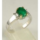 AN EMERALD RING, the oval facet cut stone claw set to shoulders each claw set with a baguette cut