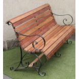 A VICTORIAN PARK BENCH of scroll back form with hard wood slatted back and seat, scrolled arms,