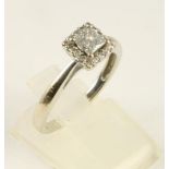 A DIAMOND CLUSTER RING, the central square cut stone within a border of sixteen pave set small