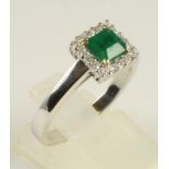 AN EMERALD AND DIAMOND RING, the square cut emerald claw set to a border of sixteen small diamonds