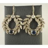 A PAIR OF DIAMOND AND SAPPHIRE PENDANT WREATH EARRINGS, the double border of leaves pave set with