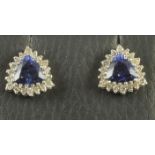 A PAIR OF TANZANITE AND DIAMOND EAR STUDS, the triangular cut tanzanite claw set to a border of