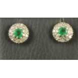 A PAIR OF EMERALD AND DIAMOND CLUSTER EAR STUDS, the circular facet cut emeralds within a white gold