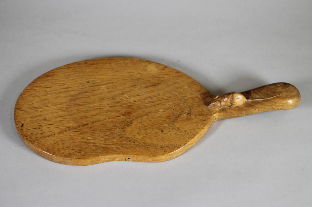 A ROBERT THOMPSON ADZED OAK CHEESEBOARD, of kidney form, the lug handle with carved mouse