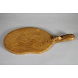 A ROBERT THOMPSON ADZED OAK CHEESEBOARD, of kidney form, the lug handle with carved mouse