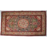 A KERMAN RUG, the navy blue field with foliate scrolls centred by a raspberry flowerhead gul,