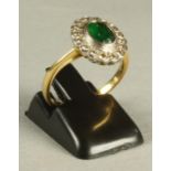 AN EMERALD AND DIAMOND CLUSTER RING, the oval facet cut emerald collet set to a border set with