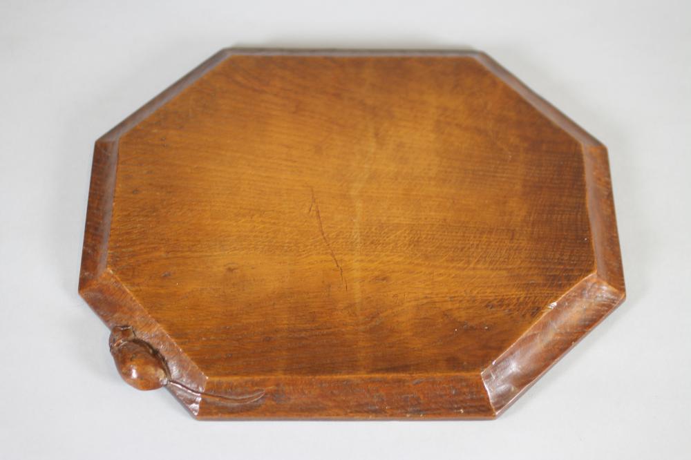 A ROBERT THOMPSON ADZED OAK BREADBOARD, of canted oblong form, the moulded edge with carved mouse