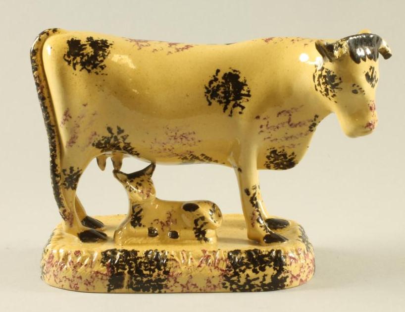 AN ENGLISH BUFF GLAZED EARTHENWARE MODEL OF A COW AND CALF, early 19th century, the horned cow