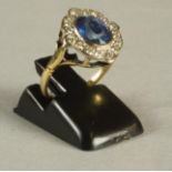 A SAPPHIRE AND DIAMOND CLUSTER RING, the oval facet cut sapphire open back collet set to a border of