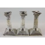 A matched set of three silver candlesticks with Corinthian capitals and turned columns on square