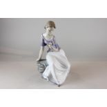 A Nao porcelain figure of a young girl sitting on a rock looking at a flower, 28cm high