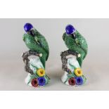 A pair of ceramic models of parrots, green glaze with blue crowns, perched on floral rocky base,