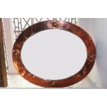 An Arts and Crafts oval mirror in beaten effect and rounded decorated frame, 63cm by 52cm