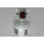 A tourmaline and diamond ring, the step cut stone rubover set within a border of mixed round cut