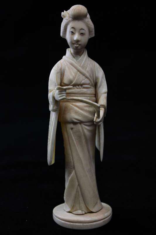 A late 19th, early 20th century Japanese carved ivory okimono of a lady in long dress holding a