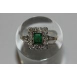 An emerald and diamond cluster ring the millegrain set stone within a border of eight cut diamonds