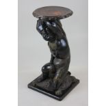 A blackamoor figure plant stand, circular top held by seated figure on a cushion and square base,