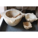 A large stone mortar and two smaller mortars with a single wooden pestle, 48cm, (NC)