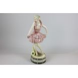 A Goldscheider porcelain figure of a girl dancing on a drum in a pink dress with a saxophone (a/