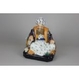 A porcelain candle holder in the form of a man with full beard and turban resting on cushions,