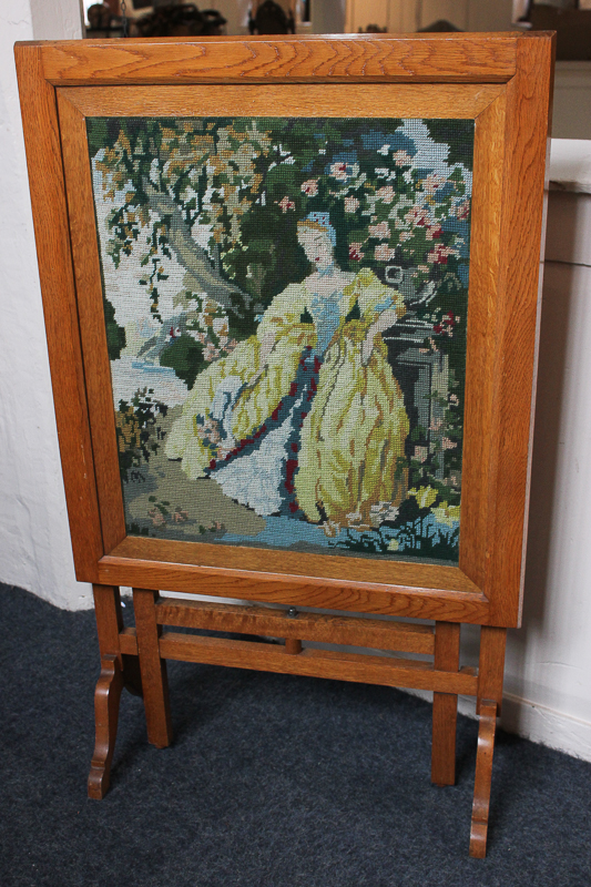 A pale oak framed fire screen with a central embroidered panel of a lady in a garden, will also