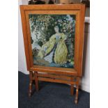 A pale oak framed fire screen with a central embroidered panel of a lady in a garden, will also