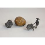 A carved nut with a winking face, a silver bird pin cushion (a/f) and a figure of a Chinese man