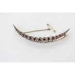 A diamond and ruby crescent brooch bead set with fifteen graduated round rubies between ribbons of