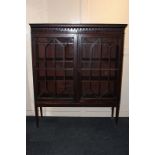 An early 20th century bookcase with panel glazed doors enclosing three shelves, on square tapered