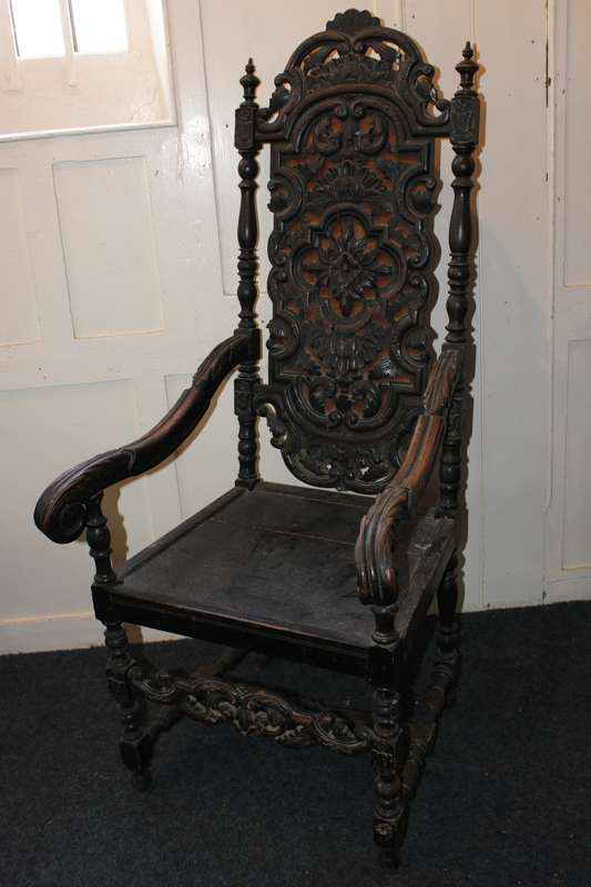 A carved oak high back chair with scroll arms and solid seat, on turned supports and stretchers (