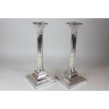 A pair of silver plated Corinthian column candlesticks on square bases with floral swag