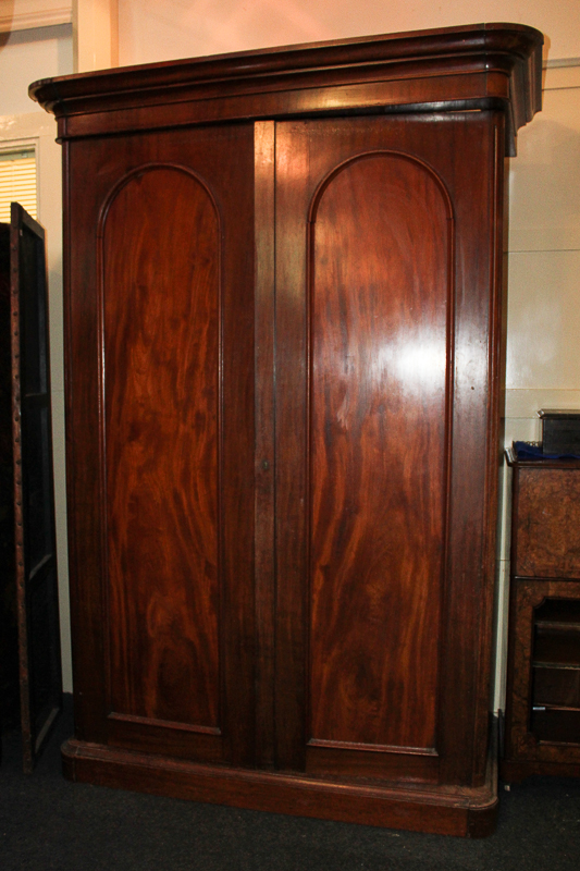 A Victorian mahogany wardrobe with two arched panel doors enclosing hanging compartment, shelves and