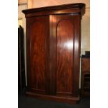 A Victorian mahogany wardrobe with two arched panel doors enclosing hanging compartment, shelves and