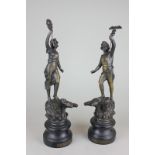 A pair of spelter figures of a male and a female youth holding an insignia, standing on the back