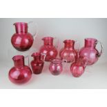 Eight Victorian and later cranberry glass jugs in various sizes