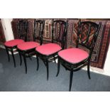 A set of four ebonised bentwood chairs with red padded seats
