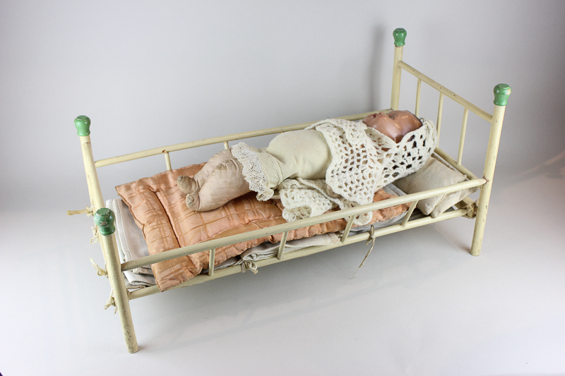A mid 20th century folding doll's bed with linen, together with a 1940's plastic and cloth doll,