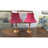 A pair of turned wood table lamps, each with red cloth shade