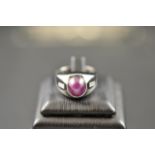 A 14k white gold ring, set with cabouchon star ruby flanked to either side with a diamond - size O,